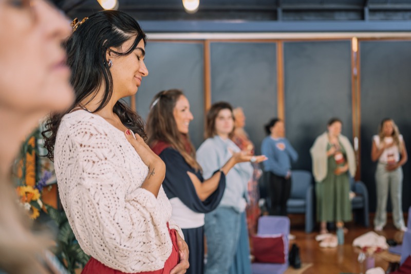 Mulheres de pé num encontro presencial com a Jade, mãos no peito